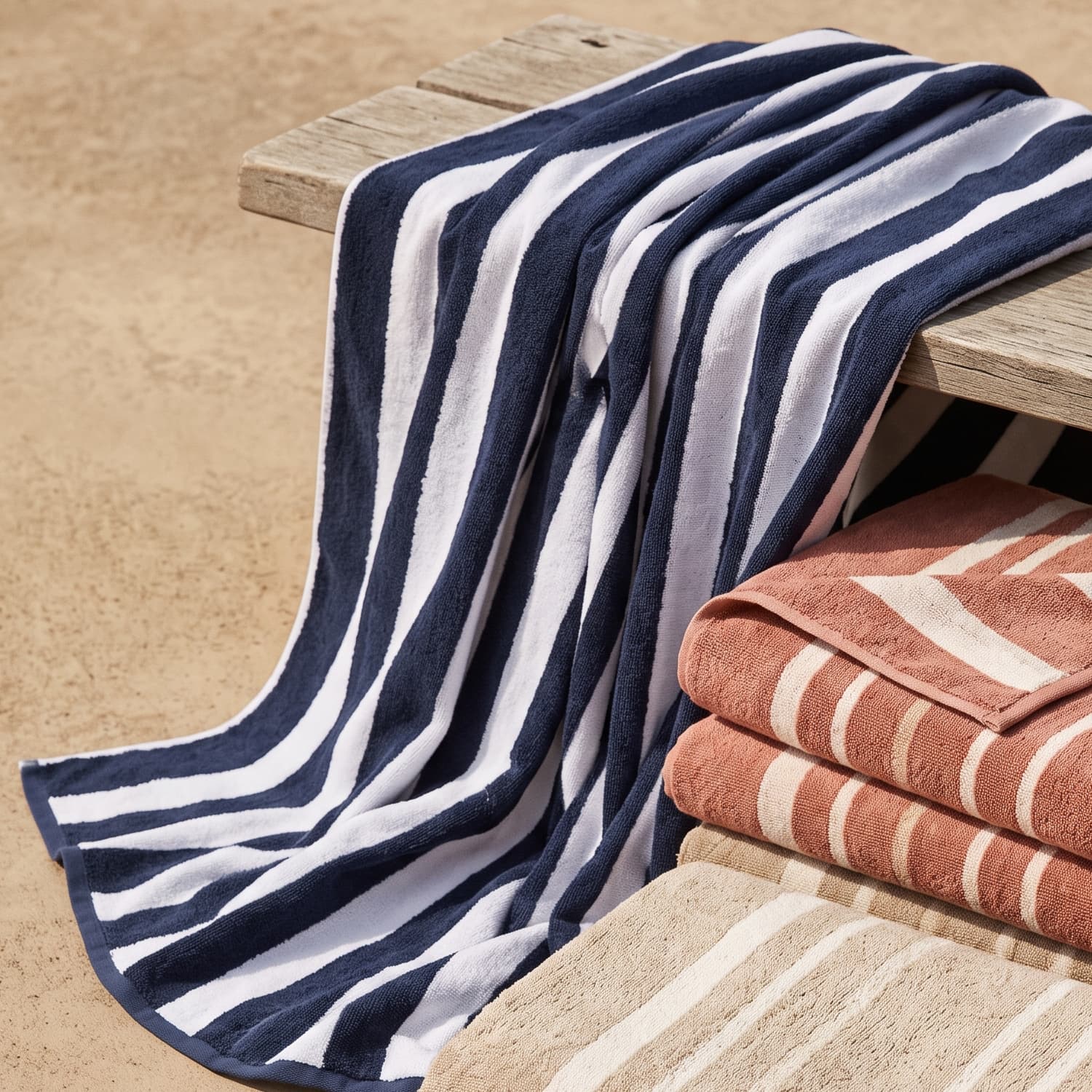 A navy and white striped cabana beach towel draped over a wooden bench