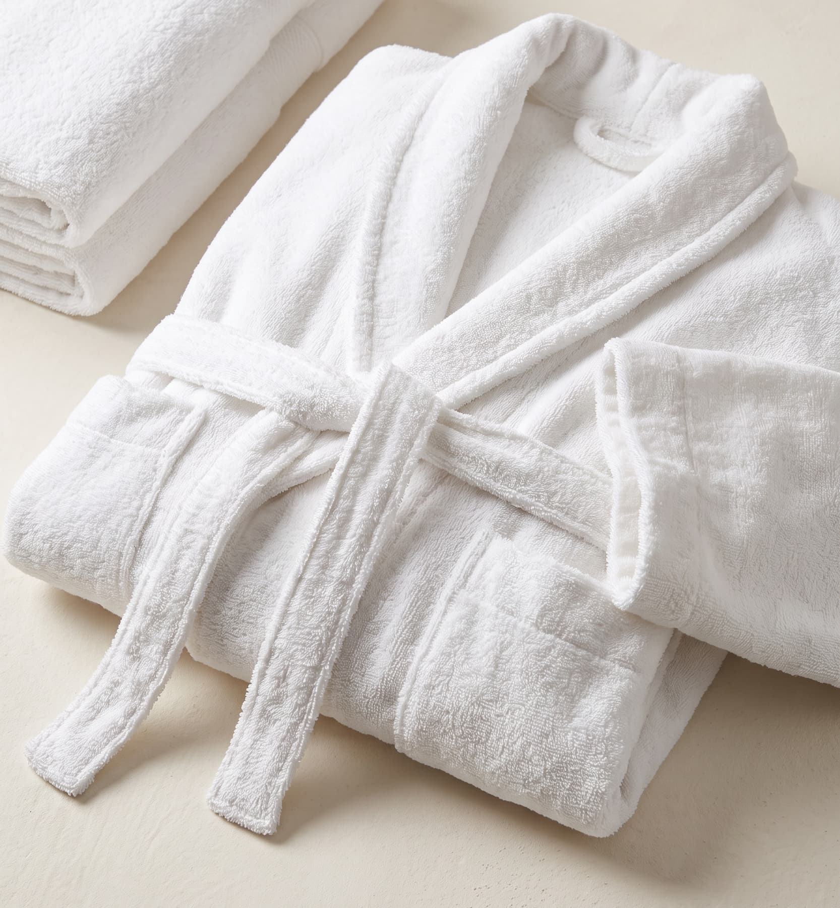 A white shawl-collar terry bathrobe folded beside matching bath towels
